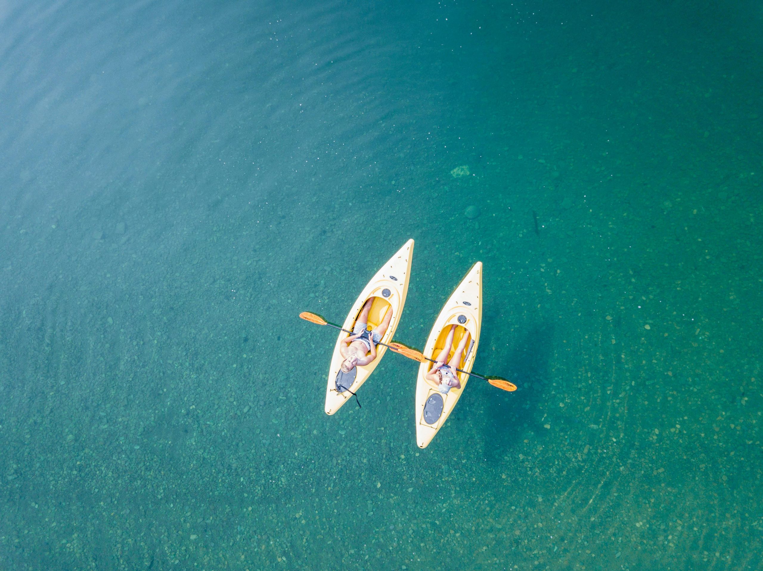 Aerial shot of two people kayaking on clear, turquoise water in a tranquil setting.